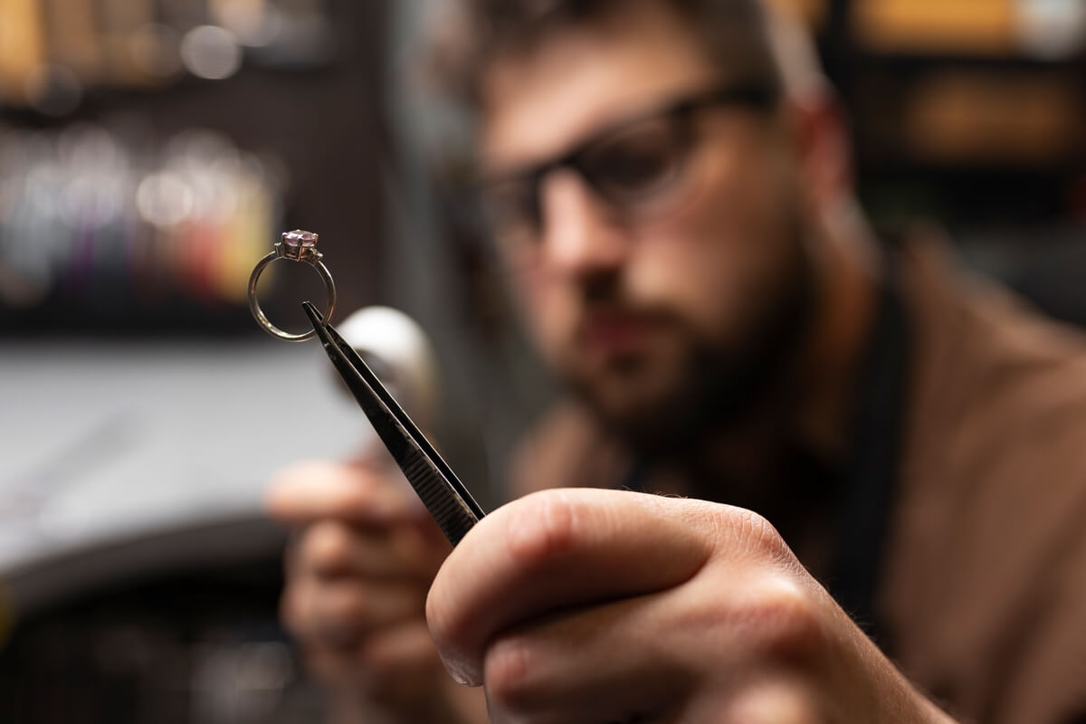 A man meticulously crafts a ring at his workstation in a jewelry shop, surrounded by tools and materials.  