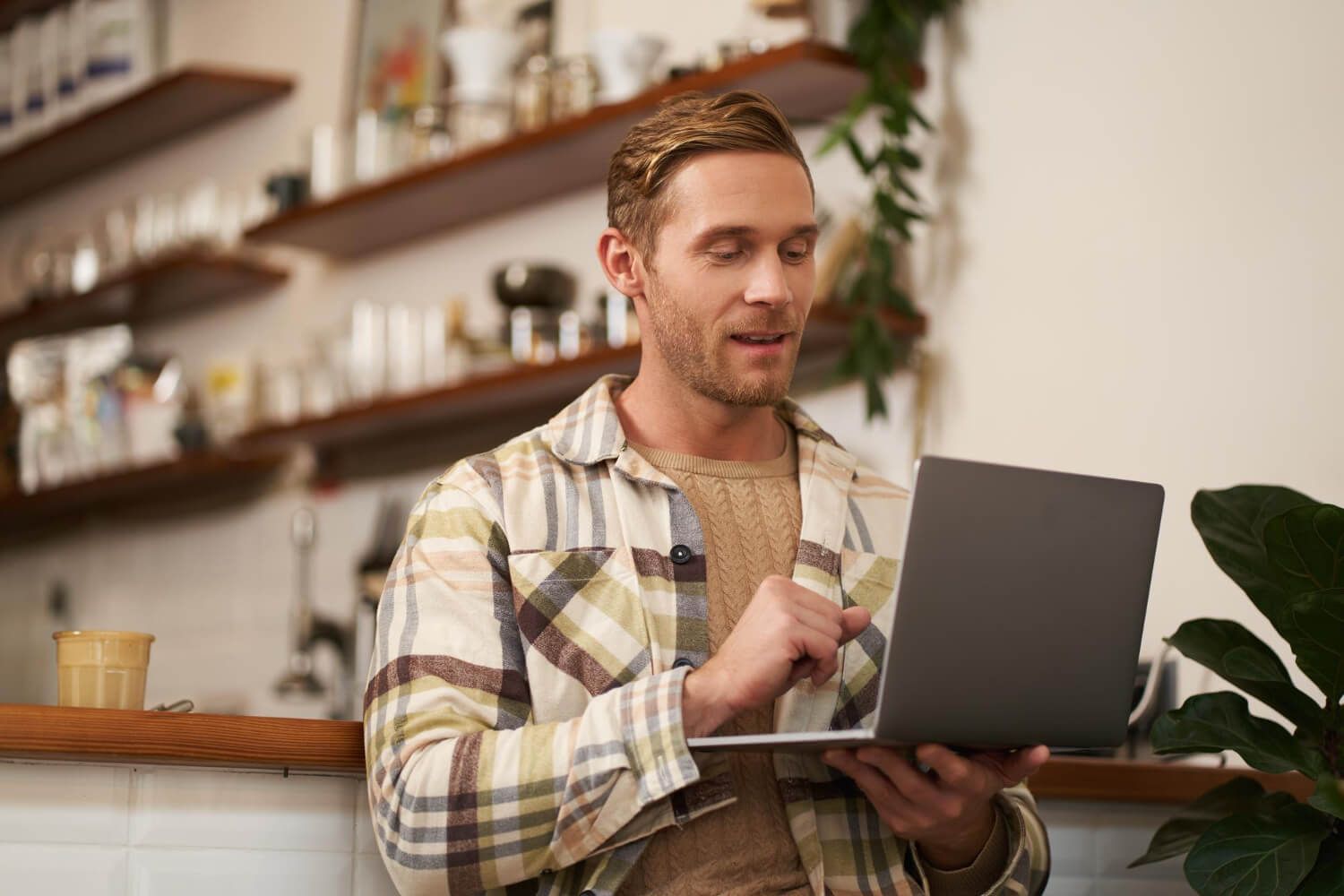 Portrait of handsome young man with laptop sitting in cafe looking at screen